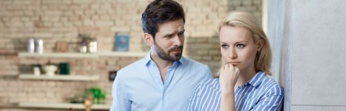 girl pissed off hand on chin while partner standing beside looking at her in kitchen