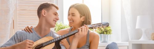 young man plays guitar happily smiles at girlfriend sitting next to