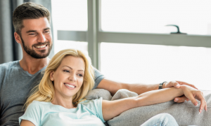 couple sitting on white coach smiling hand in hand in living room