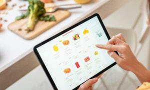 woman shopping online for healthy fruits beside healthy vegetables bowl broccoli on chopping board on table