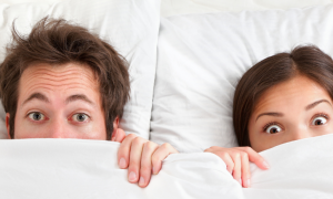 couple lies on white pillows starring covering face with big white blanket