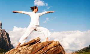 woman stood on rock practicing yoga in blue cloudy sky