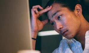 man hand on forehead stressed thinking looking at personal computer