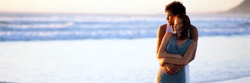 couple stood near beach hugging each other in shining sky