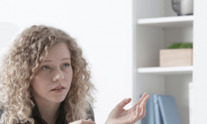 young woman with short curly blonde hair looks at man talking white drawer behind