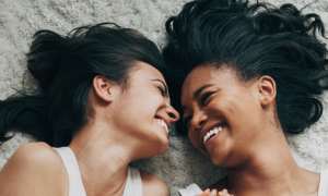 two girls lies on white fluffy carpet smiles at each other