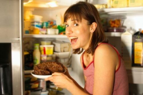 Woman eating unhealthily by sneaking into the fridge