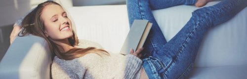 girl eyes closed happily smiling lying on white couch holding book