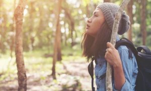 young woman holds tree stick hiking in forest