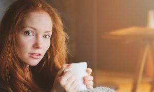 woman sits in office room holds white mug drinking