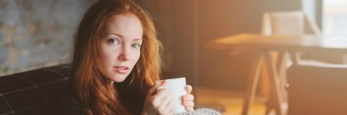 woman sits in office room holds white mug drinking
