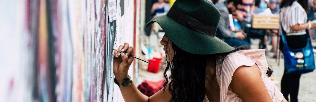 long curly black hair woman with green hat joins gravity paints on street wall