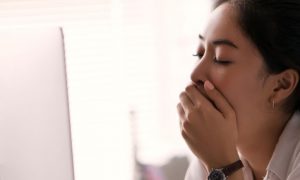 woman hand covering mouth feeling sleepy tired when looking at laptop