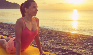 middle aged woman practices yoga on yellow yoga mat beside beach
