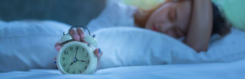 Girl hand on head holds white clock sleeps beside white pillows