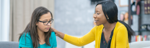 A woman resting a reassuring hand on a friend's shoulder, supporting her mental wellbeing