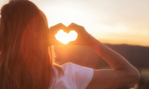 Woman facing the golden sunset making a love heart shape