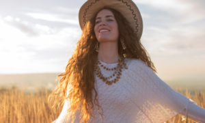 Beautiful young woman with a straw hat and a white poncho smiling and enjoying the sun in the middle of the grass field.