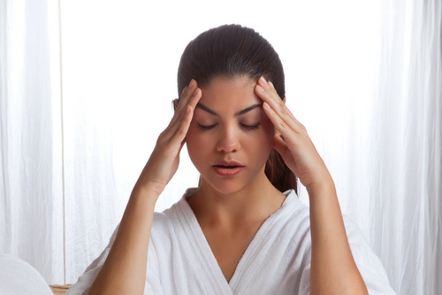 Expressive image of a young woman with a headache massing her temples