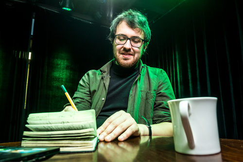 Creative person, writer and screenwriter sits at a table and sings in a notebook and laptop on a green background