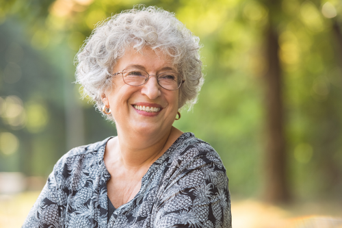 Portrait of smiling elderly woman with eyeglasses at park. Laughing senior woman looking away. Happy thoughful mature woman relaxing outdoor. Old active retired woman.