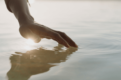 persons hand touching the ocean in beautiful light