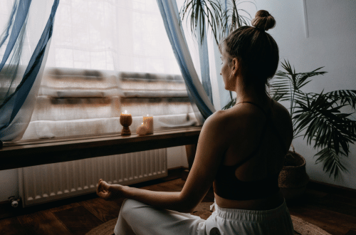woman with a bun in her hair sitting at a window meditating