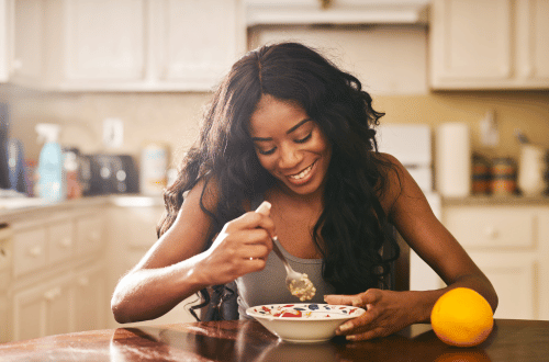 Woman in the kitchen eating a healthy breakfast with an orange.