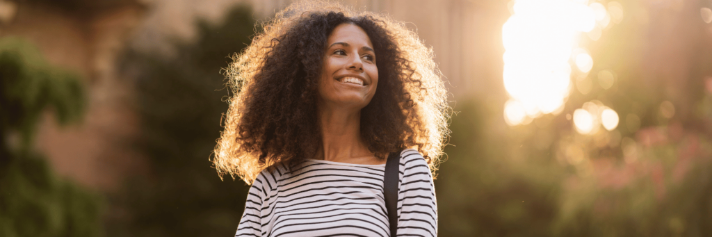 Happy empowered woman with long frizzy black hair in the sunshine