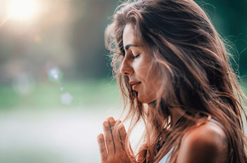 Woman with long hair and hands in prayer position, feeling the benefits of meditation.