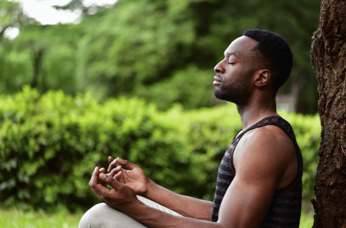 Man quietly meditating against a tree,  feeling the benefits of meditation.