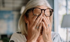 A woman sitting on her sofa with her eyes closed and her head resting on her hand, showing emotional exhaustion signs