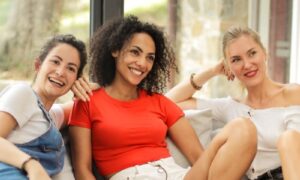 Three friends laughing together on a bright sofa, collective energy at its best