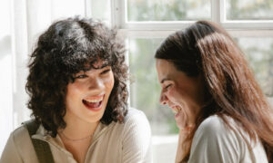 Two women in their forties laughing together in a bright, light-filled room, showing emotional resonance at its best