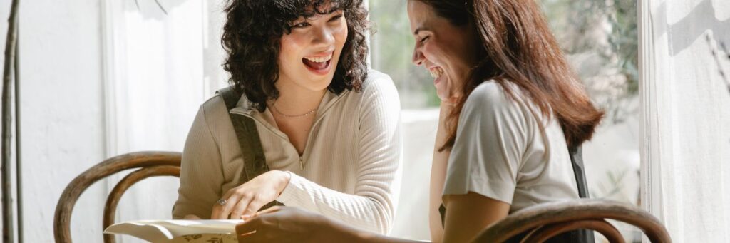 Two women in their forties laughing together in a bright, light-filled room, showing what ease looks like when rejection sensitivity has settled