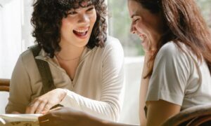 Two women in their forties laughing together in a bright, light-filled room, showing what ease looks like when rejection sensitivity has settled