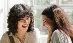 Two women in their forties laughing together in a bright, light-filled room, showing emotional resonance at its best