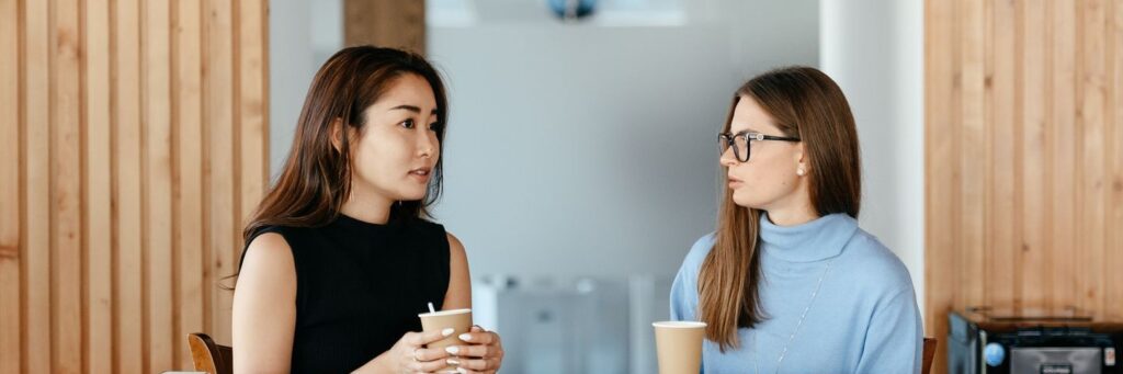 A manager and colleague talking calmly over coffee, working through job demands together