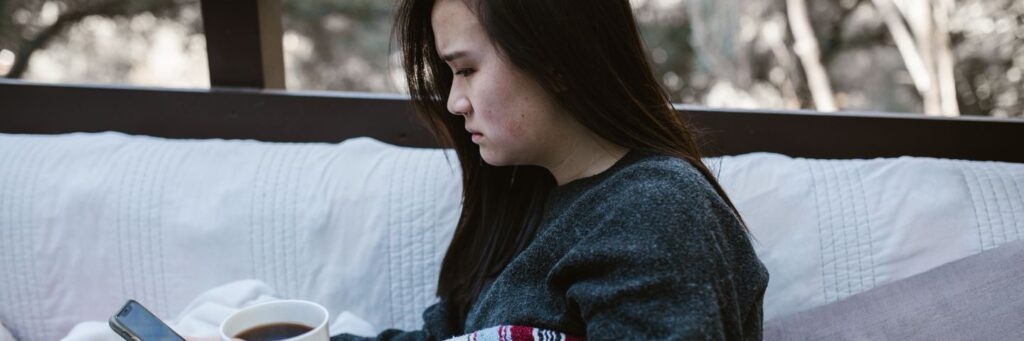 A woman wrapped in a blanket re-reading a message on her phone, a quiet picture of fear of abandonment