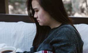 A woman wrapped in a blanket re-reading a message on her phone, a quiet picture of fear of abandonment