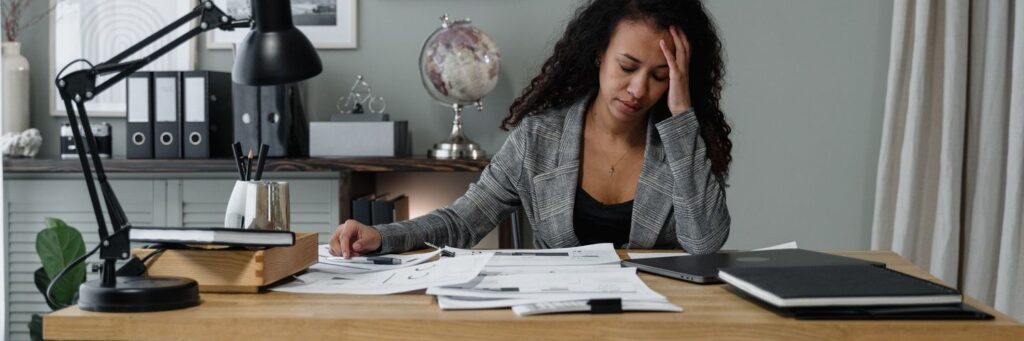A woman with her hand to her forehead at a desk covered in paperwork, showing why managing job demands at work matters
