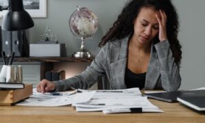 A woman with her hand to her forehead at a desk covered in paperwork, showing why managing job demands at work matters