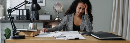 A woman with her hand to her forehead at a desk covered in paperwork, showing why managing job demands at work matters