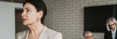 A woman in her fifties listening closely to a colleague across a meeting table in a bright modern office