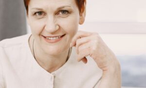 A woman in her forties smiling calmly by a sunlit window at home, showing what nervous system regulation feels like day to day