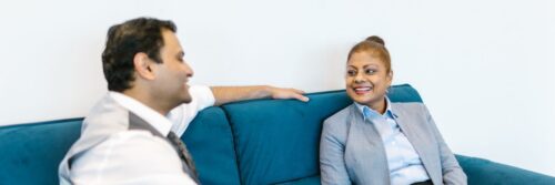 A manager and colleague talking easily on a teal sofa in a bright office, a workplace where psychosocial hazards are managed well