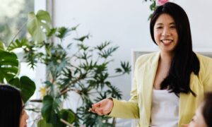 A smiling leader in a yellow blazer talking with her team in a bright office, trauma-informed leadership in action