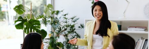 A smiling leader in a yellow blazer talking with her team in a bright office, trauma-informed leadership in action