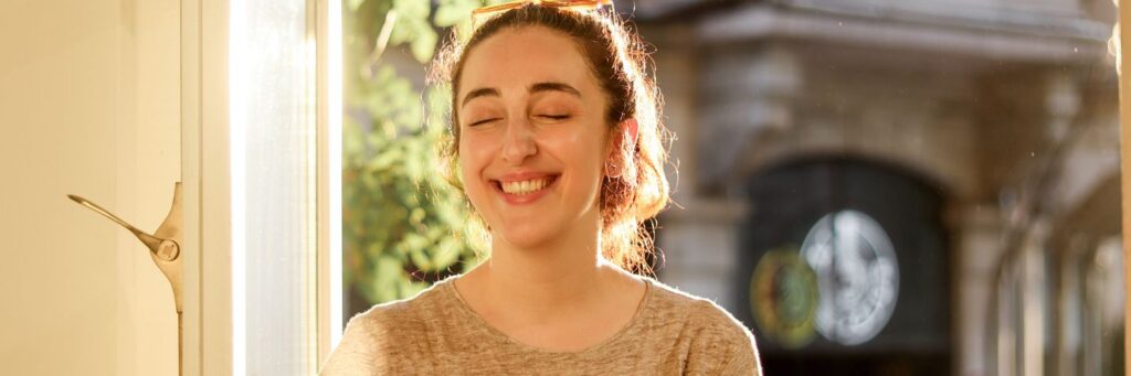 A woman in her forties smiling calmly by a sunlit window, showing life after recovering from chronic stress effects