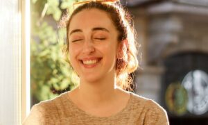 A woman in her forties smiling calmly by a sunlit window, showing life after recovering from chronic stress effects